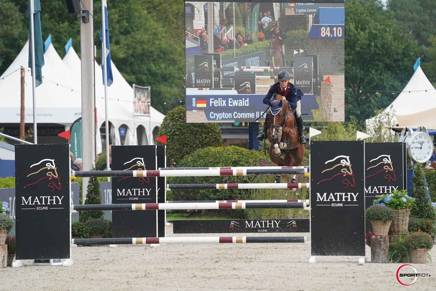 Felix Ewald na konju Crypton Comme Il Faut skače preko Mathy prepona na međunarodnom preponskom natjecanju, s velikim ekranom i publikom u pozadini.