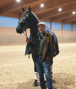 Muškarac stoji iza Longines prepona na konjičkom stadionu s praznim plavim i bijelim tribinama u pozadini.